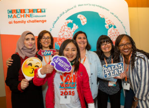 A group of women pose in front of a sign saying "AI Family Challenge" at the Ai Family Challenge World Championship