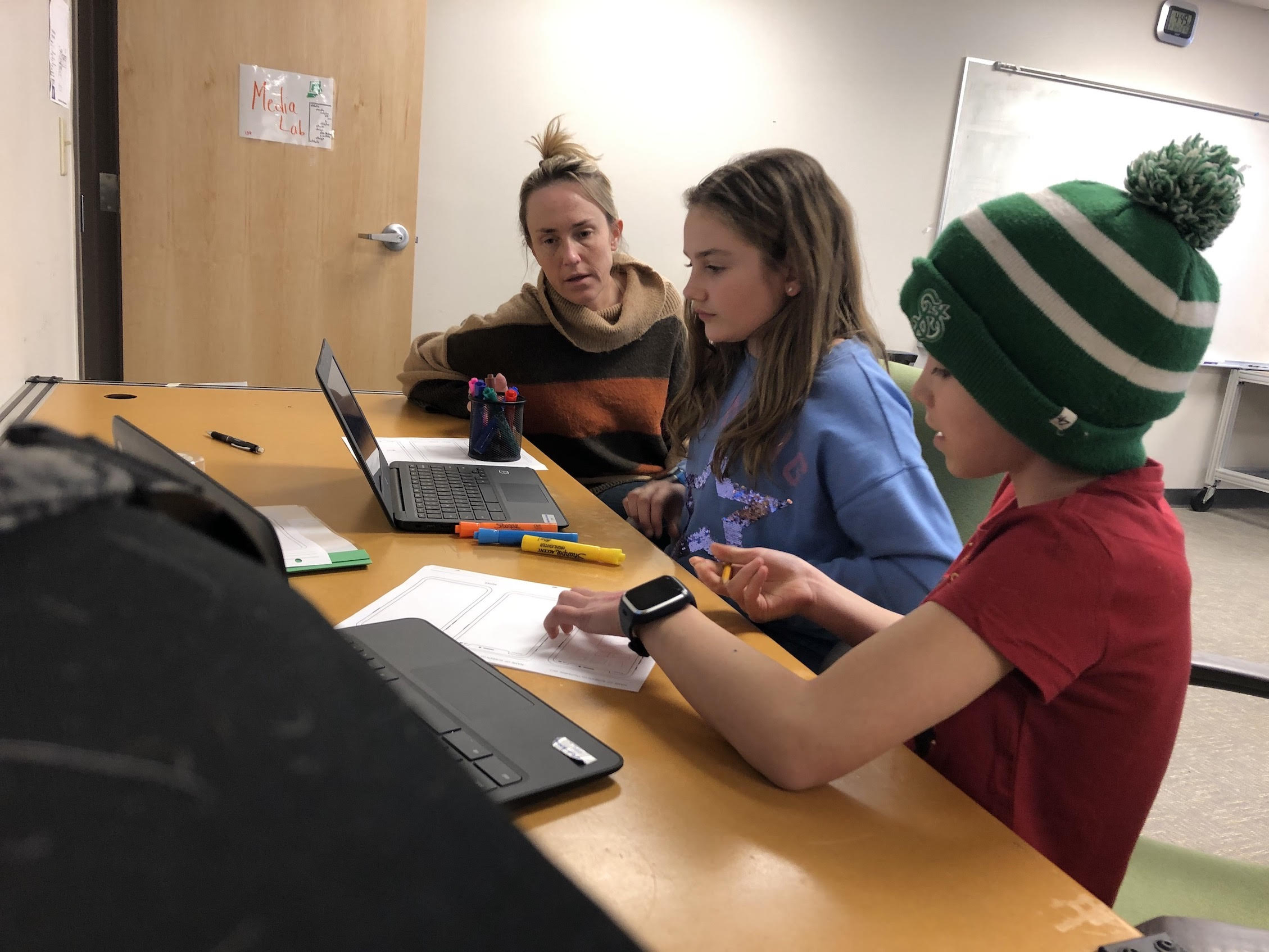 A young woman mentors two young girls at a desk with two laptops