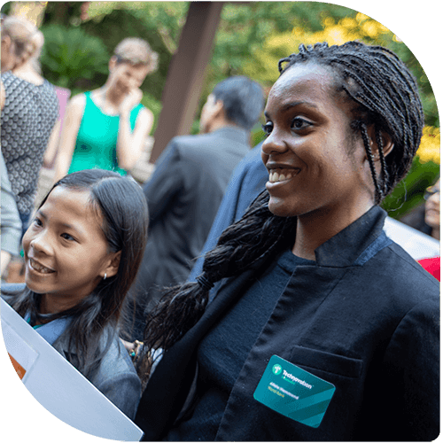 A professional woman smiling with her arm around her mentee, who is a young girl from Cambodia who has just presented her app prototype at a Technovation event